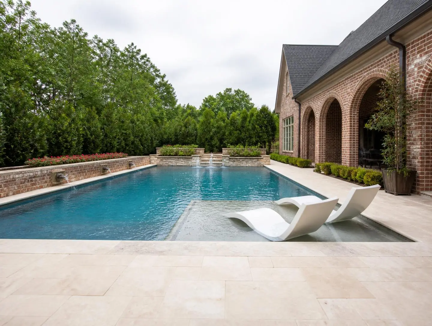 Rectangular gunite pool with tanning ledge and travertine deck behind a brick home